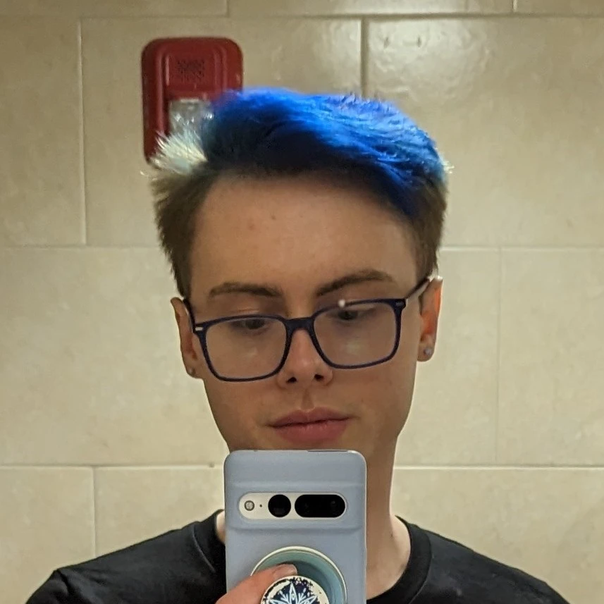 Selfie of the website creator, Nick Cipriani with bright blue dyed hair and blue glasses, holding a Pixel 6 Pro with a blue case and a blue Christmas themed PopSocket magnetically attached.